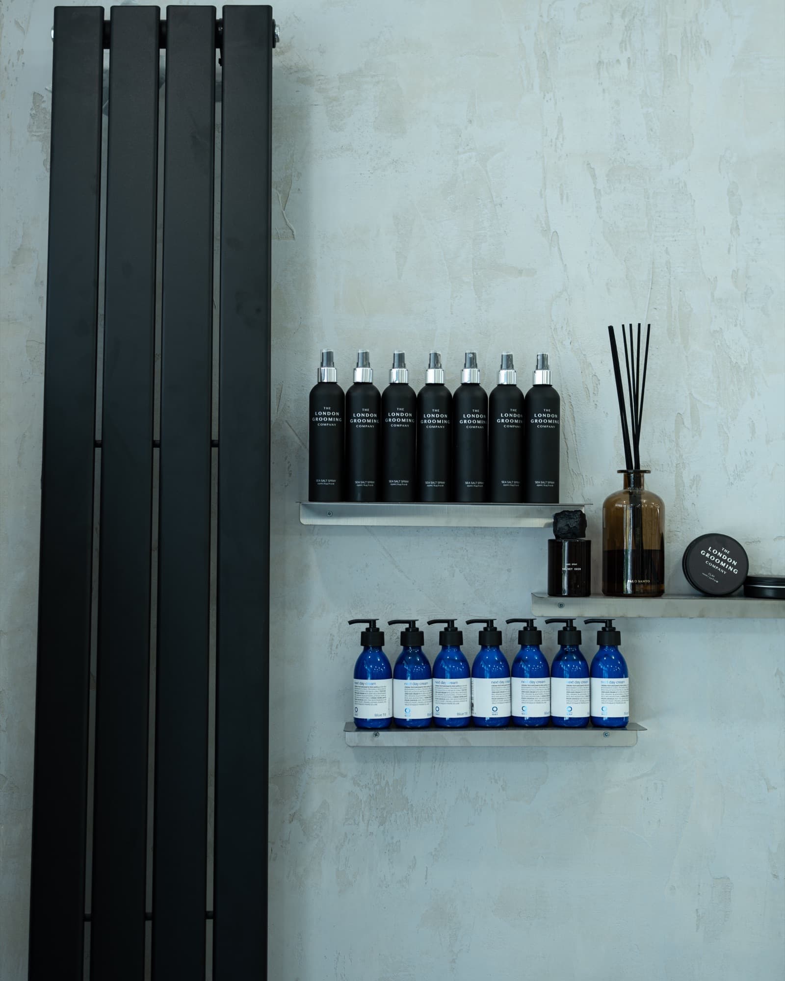 Półka w studio FRIME — niebieskie butelki OWAY next day cream i czarne produkty London Grooming
