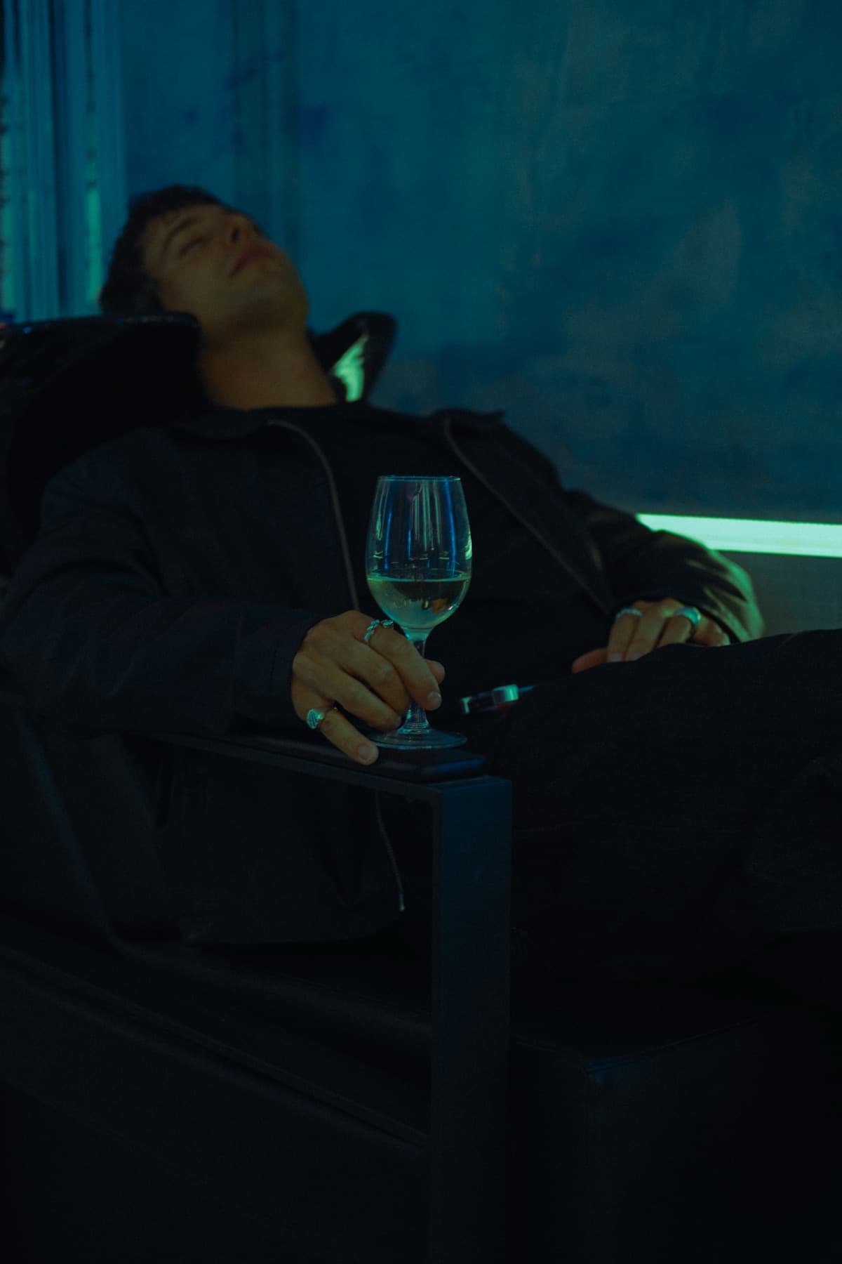 Gość z lampką wina na fotelu w niebieskim świetle studia